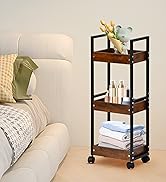 Chariot roulant à trois niveaux avec étagères en bois et cadre en métal noir. L'étagère supérieure contient un vase avec des fleurs, l'étagère du milieu contient des bouteilles de cosmétiques, l'étagère inférieure contient des serviettes pliées.